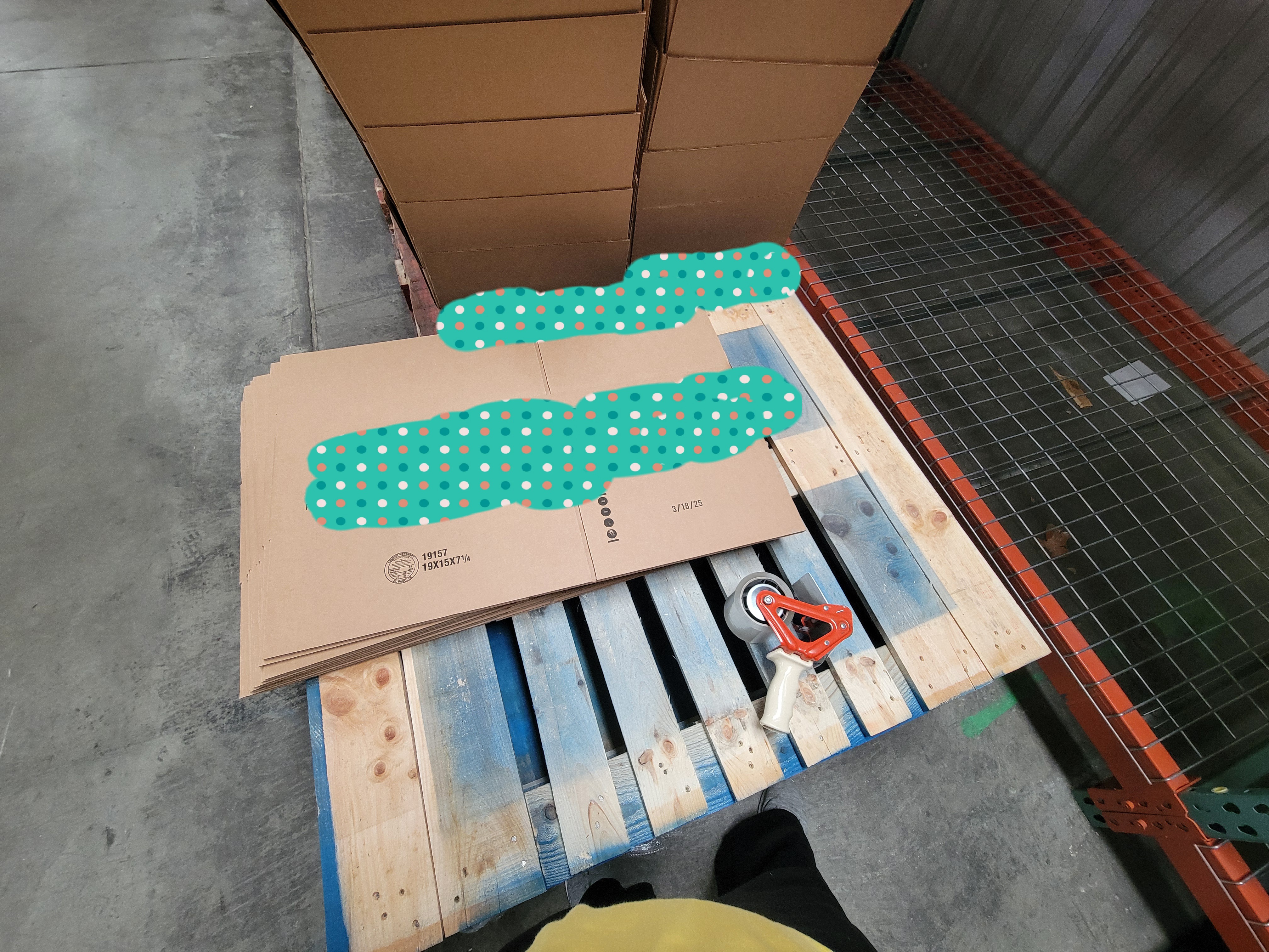 Flattened boxes and tape gun on a pallet with put together boxes on another pallet next to it.